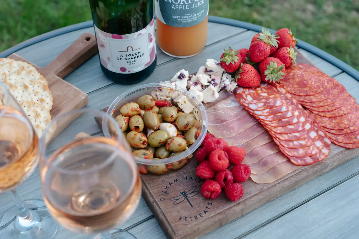 A grazing board with charcuterie, olives, strawberries and two glasses of rosé